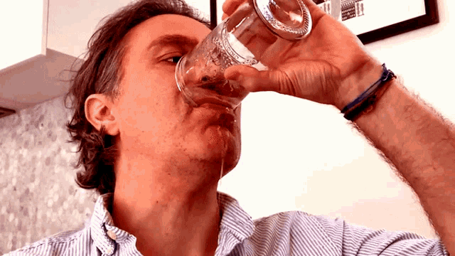 a man in a striped shirt drinks from a glass with a picture on the wall behind him