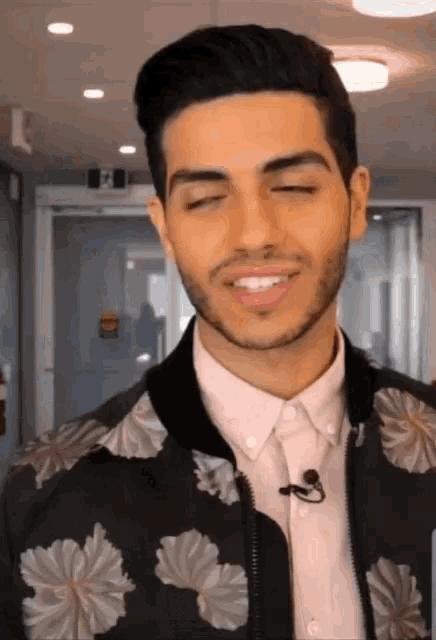 a man wearing a floral jacket and a pink shirt is smiling with his eyes closed