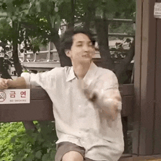 a young man is sitting on a bench in front of a no smoking sign and smoking a cigarette .