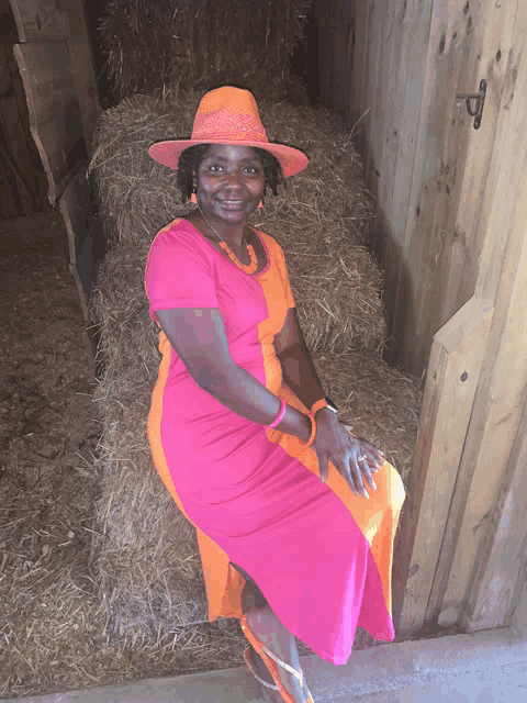 a woman in a pink dress and orange hat sits on a bale of hay