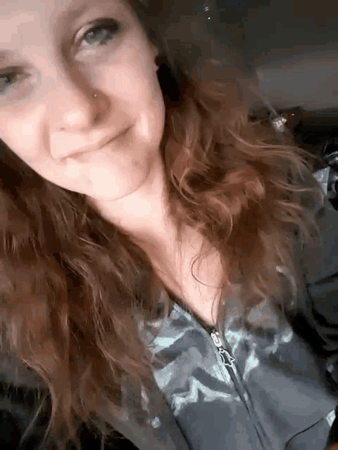 a woman with long red hair and a nose ring is smiling for the camera .