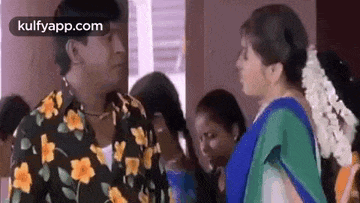 a man in a floral shirt is talking to a woman in a blue sari .