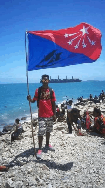 a man in a red shirt with the word pm on it holds a flag