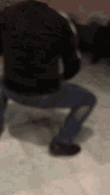 a man in a black shirt and blue jeans is squatting down on the floor .