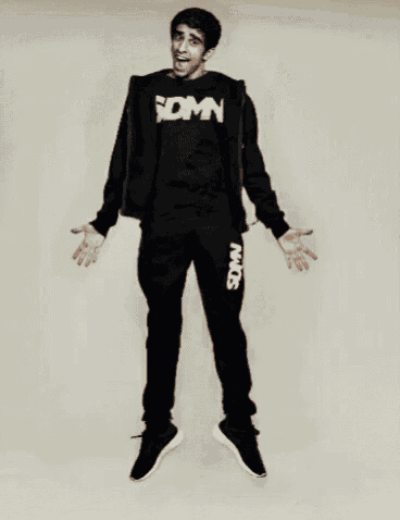 a man wearing a sdmn shirt is jumping in the air with his arms outstretched