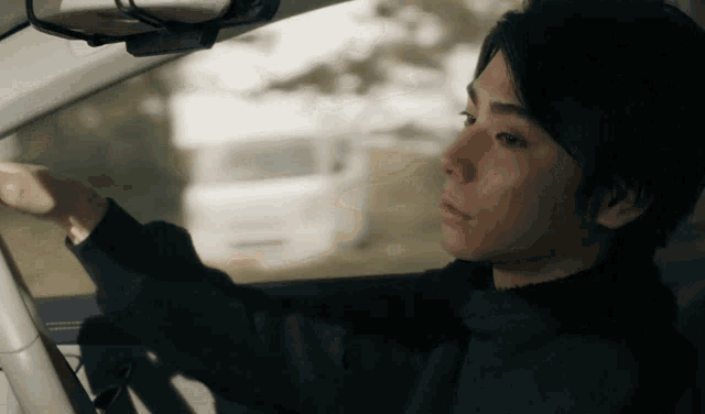 a man in a black sweater is driving a white car
