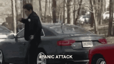 a police officer is standing next to a car in a parking lot and says panic attack .