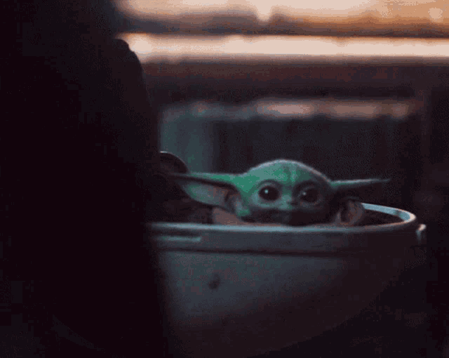 a baby yoda is sitting in a bucket in a dark room