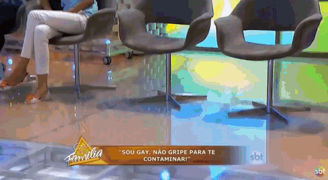 a woman sits in a chair in front of a sign that says " sou gay não gripe para te contaminar "