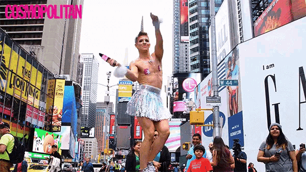 a man dressed as a unicorn is dancing in a crowded city street with a cosmopolitan ad in the background