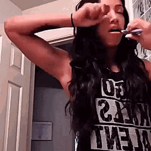 a woman brushing her teeth wearing a shirt that says ' twenty ' on it