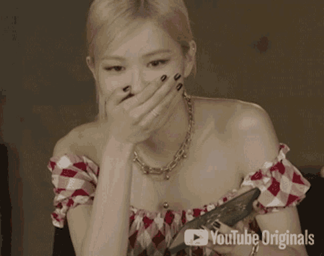 a woman covering her mouth with her hand while holding a cell phone with youtube originals written below her