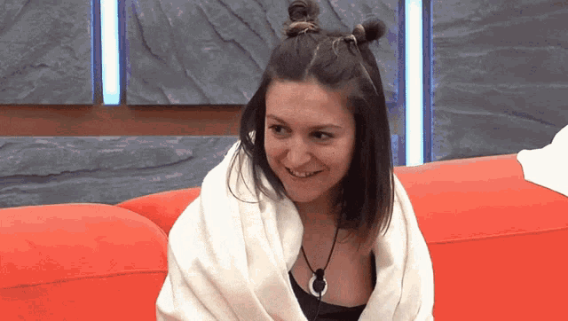 a woman wrapped in a white blanket is smiling on a red couch