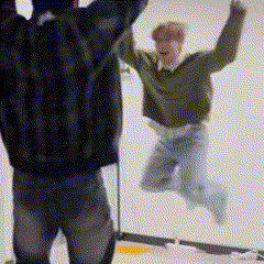 a man in a green sweater is jumping in the air while another man watches .