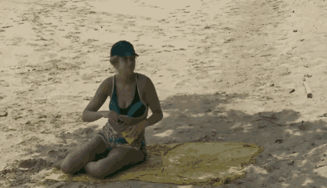 a woman in a bikini sits on a towel on the beach