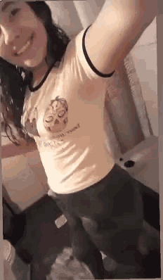 a woman is taking a selfie in a bathroom while wearing a yellow t-shirt and black pants .