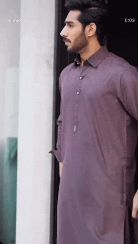 a man in a purple shirt is standing in front of a window