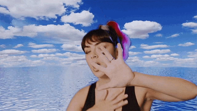 a woman covering her face with her hand in front of a blue sky with clouds