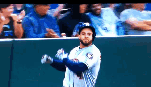 a baseball player wearing a helmet and gloves is standing in front of a crowd .