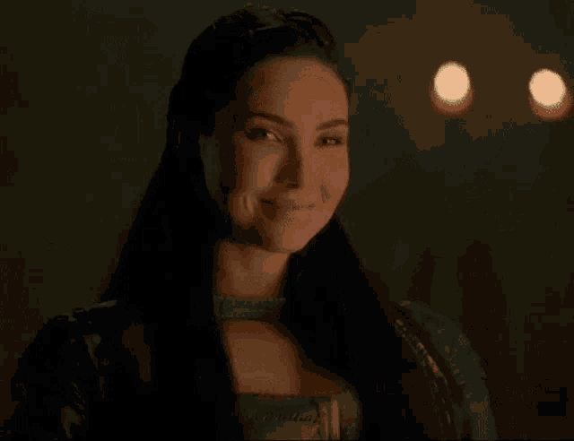 a woman with long dark hair is smiling in a dark room with candles in the background .
