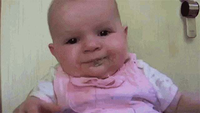 a baby in a pink dress is making a sad face .