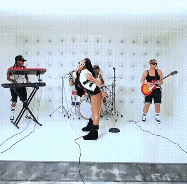 a woman sings into a microphone while a man plays a keyboard and a woman plays a guitar