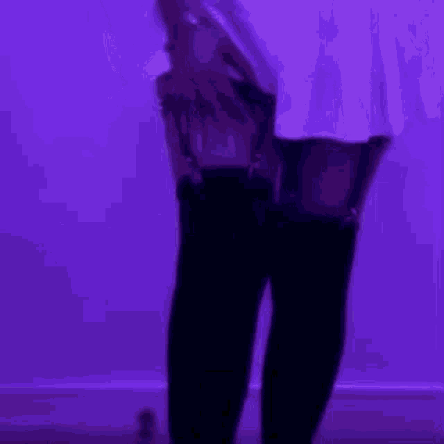 a woman in a white pleated skirt and black thigh high stockings is standing in front of a purple wall .
