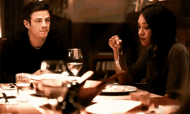a man and a woman are sitting at a table with plates of food and wine glasses .