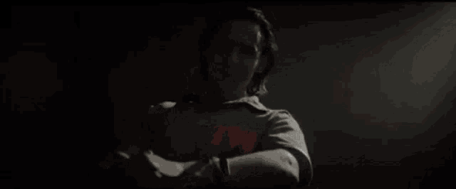 a man is standing in a dark room wearing a shirt with a red t on it .