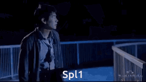 a man in a suit is standing in a dark room with the words spl1 written on the screen .