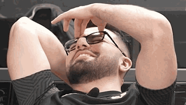 a man with a beard and glasses is laying down with his hands behind his head
