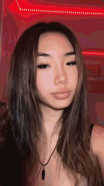 the girl is wearing a necklace and taking a selfie in front of a red background .