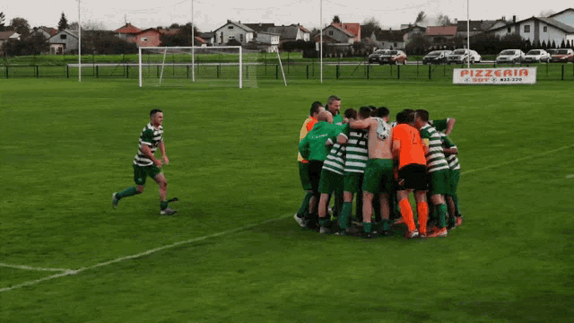 a group of soccer players huddle on a field with a pizzeria sign behind them