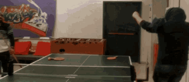 a man playing ping pong with a hoodie on