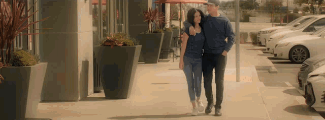 a man and a woman are walking down a sidewalk in front of a parking lot