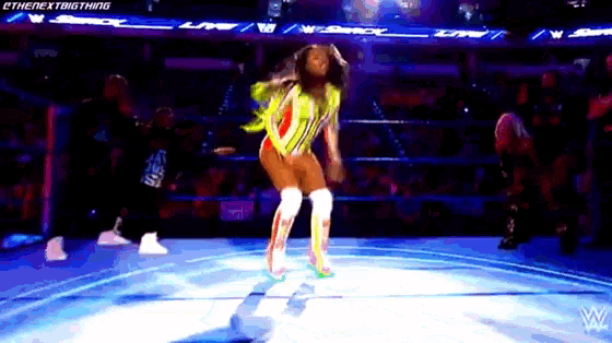 a woman in a yellow outfit is dancing on a stage in front of a wrestling ring ..
