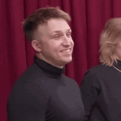 a man in a black turtleneck stands next to a woman in a black sweater