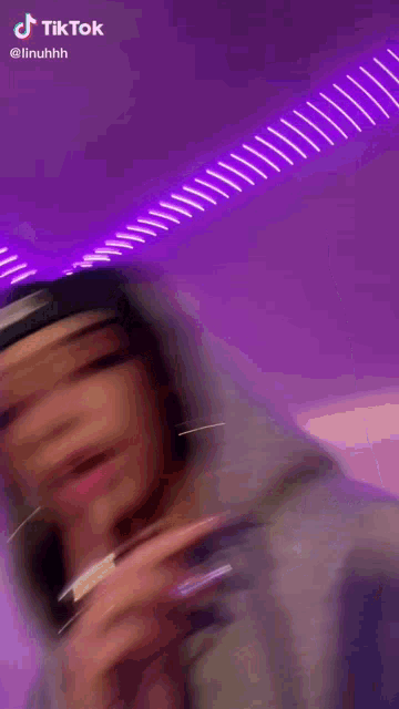 a woman wearing a hat and a hoodie is smoking a cigarette in front of a purple background .