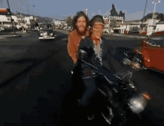 two men are riding a motorcycle down a street in front of a gas station .