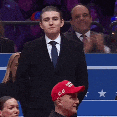 a man in a suit and tie is wearing a hat that says make america great again