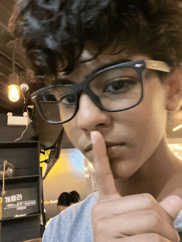 a boy wearing glasses holds his finger to his lips