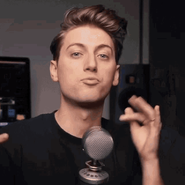 a young man in a black shirt stands in front of a microphone making a funny face
