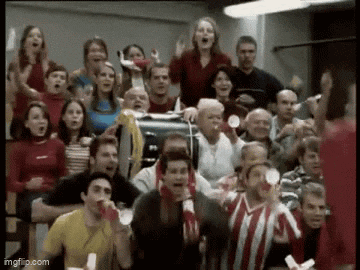 a large group of people are sitting in a stadium watching a game and cheering .