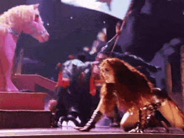 a woman is kneeling down in front of a pink horse on a stage