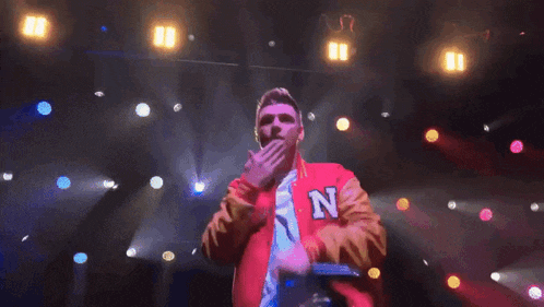 a man in a red jacket is singing into a microphone on a stage