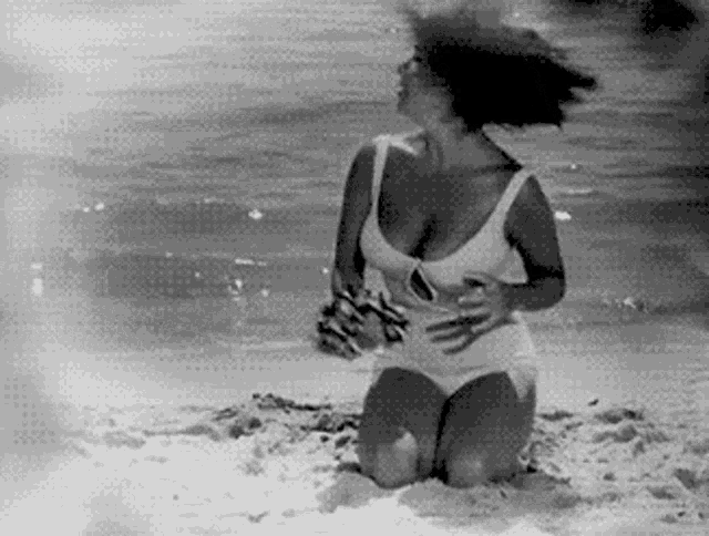 a woman in a bathing suit is kneeling in the sand on the beach .