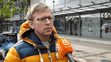 a man wearing glasses is being interviewed by someone with a tv vest microphone