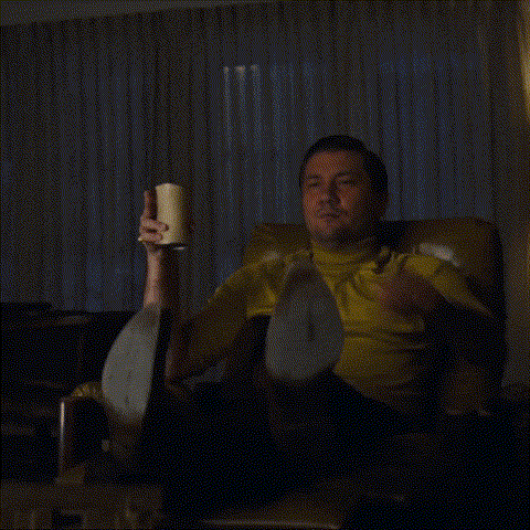 a man in a yellow shirt sits in a chair holding a cup and pointing