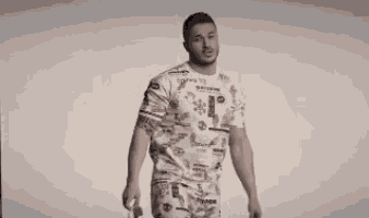 a man wearing a t-shirt and shorts is standing in front of a white background and smiling .