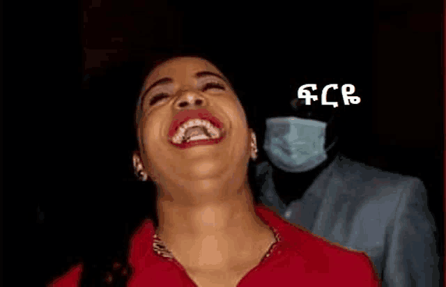 a woman in a red shirt is laughing with a man wearing a mask behind her .